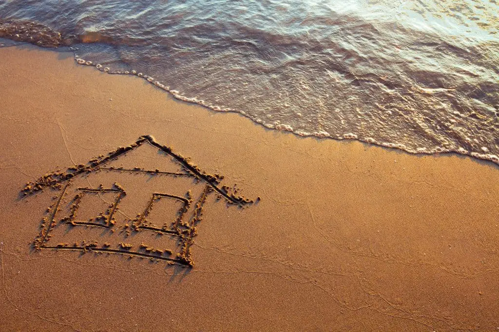 Drawing of a simple house in the sand with water lapping nearby 