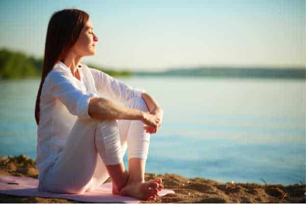 Woman meditating on the beach.  Christian meditation sitting with hands clasped together.