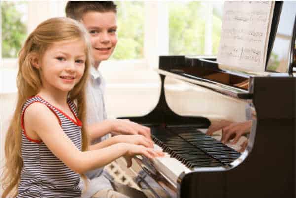 girl and boy playing hymns on a piano