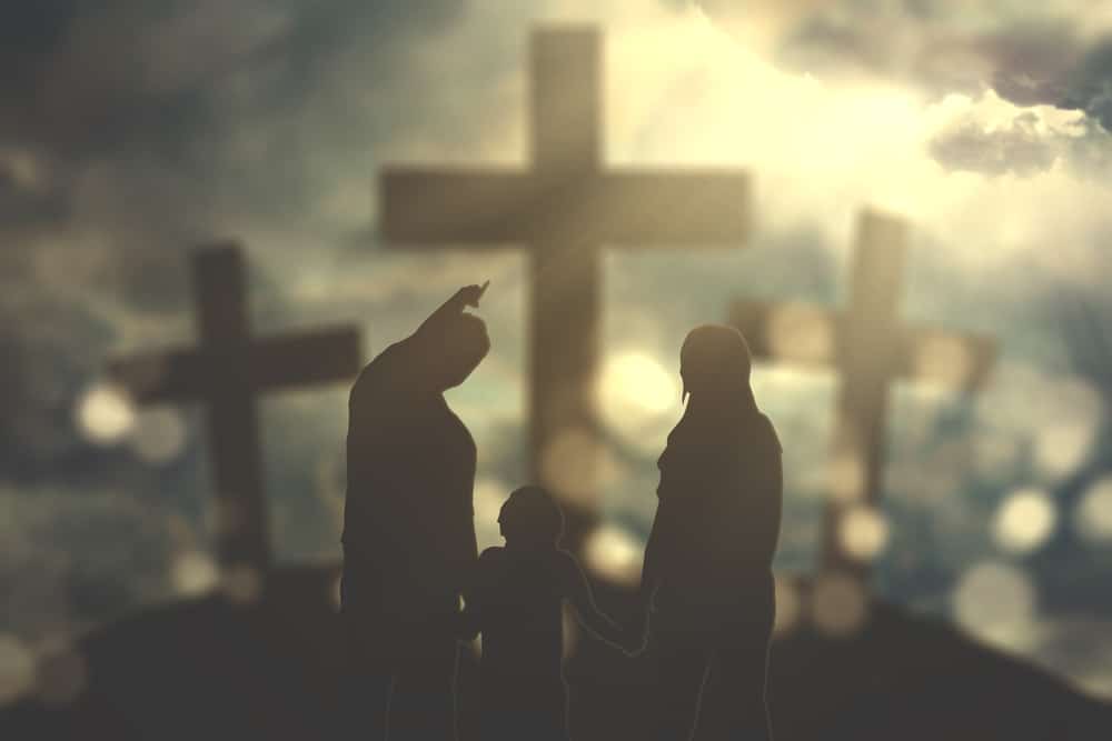 Three crosses in the background, blurred with blues and browns.  A family in the foreground - father, mother and child.  After a child is ready to be baptized, they still need to be pointed to Christ.  The father in the picture is pointing to the cross. 