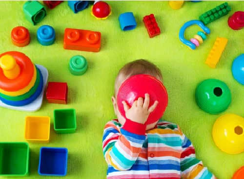 Child laying on the floor in stripped play outfit surrounded by toys. Parent is wondering how to teach kids to declutter biblically. 