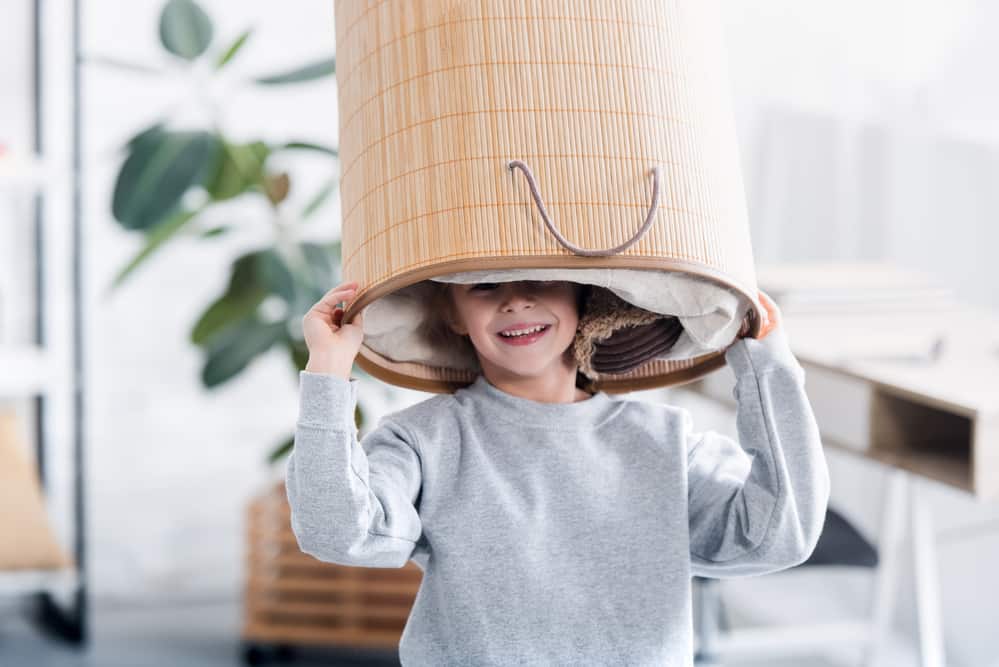 Happy little young man holding a laundry basket over his head - he is helping out because it is a smart mom laundry hack and tip. 