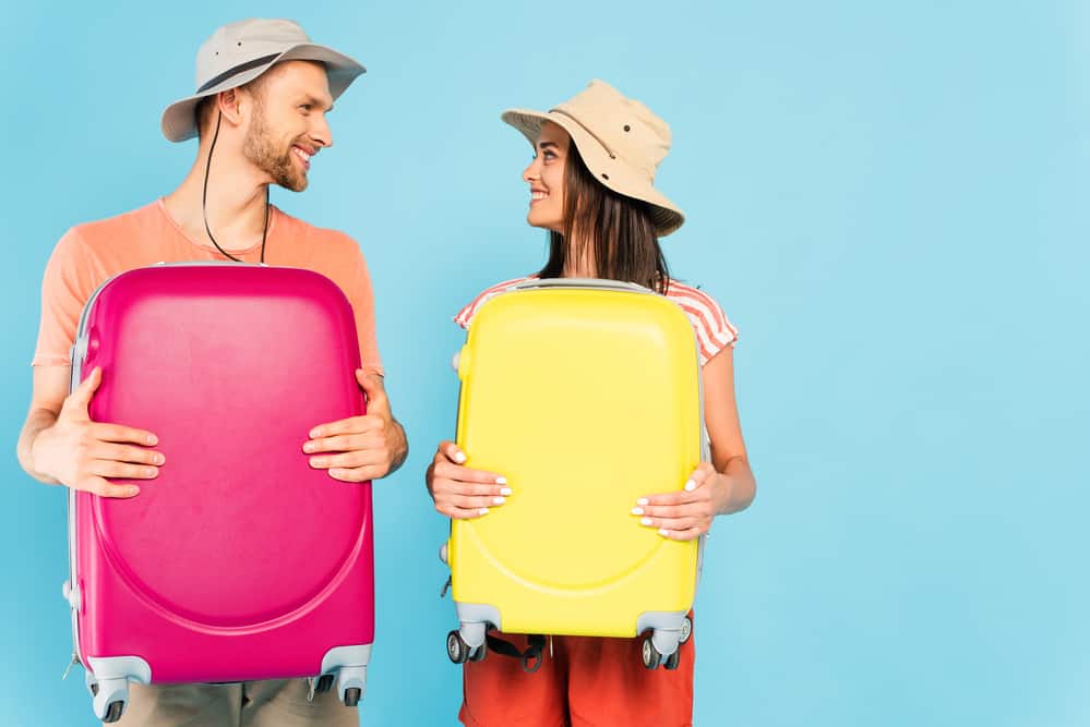 Couple holding colorful luggage and smiling at each other.