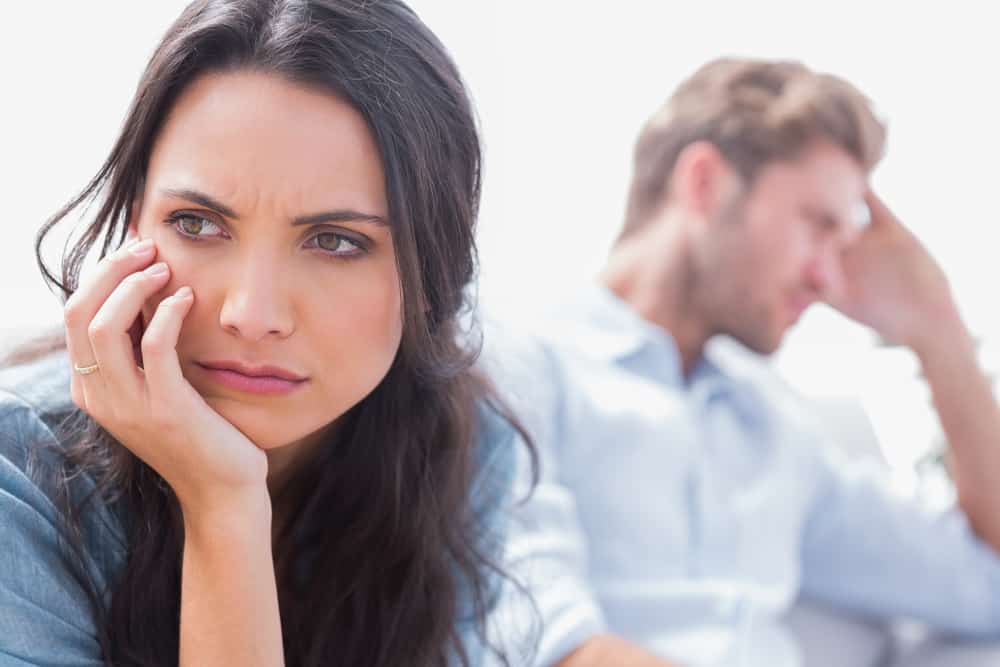 Couple having an obvious disagreement. Man in the background with head in hands.  Woman in front with sad face. Obviously in need of Christian marriage counseling. 