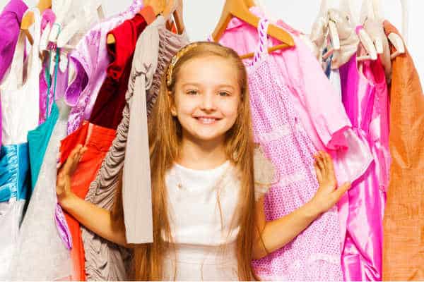 Child trying to get ready for church but overwhelmed by too many choices. She needs to get dressed for church but she is standing in the middle of a rack of clothes.