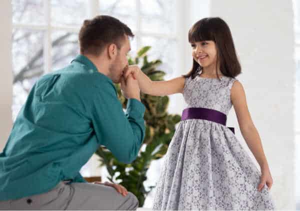 Young girl is getting dressed for church and her dad is holding her hand and kneeing in front of her in approval.  