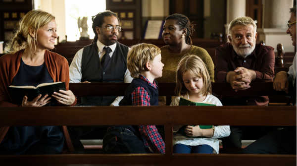 Kids dressed for church and sitting with their parents in the pew.  Other adults behind them are getting ready for church. 