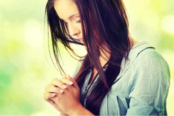 Closeup portrait of a young caucasian woman praying, against abstract green background - how to pray without ceasing