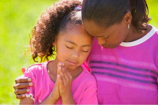 Black mother praying with her black daughter.  Both in purple and pink shirts. Serene and peaceful picture - pray without ceasing