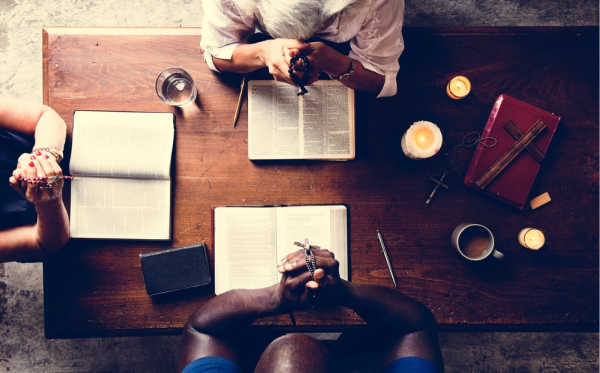 Diverse gathering of three Christians praying with their Bibles open in front of them. 