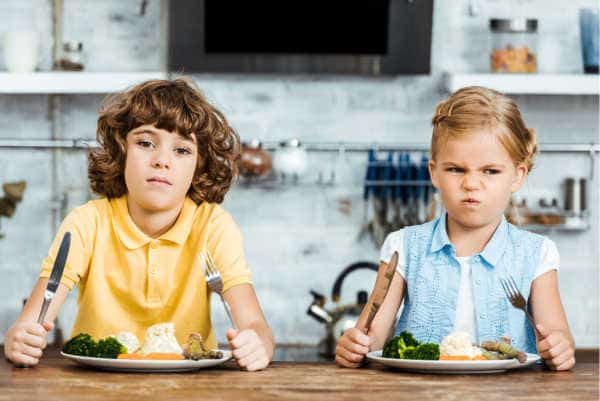 Two kids with forks and knives raised and full plates of yummy food with mad and frustrated faces - just like when God's kids complained about their food too