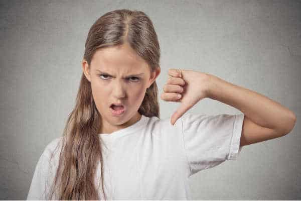 Young preteen girl in white shirt with a face of disgust and her thumb pointed down - she is complaining and grumbling - just like God's kids complained about his cooking