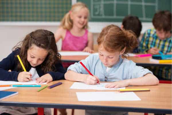 Two young girls working hard in class at school sitting side by side at a desk working on their projects because real school is importance but we wonder about the importance of sunday school