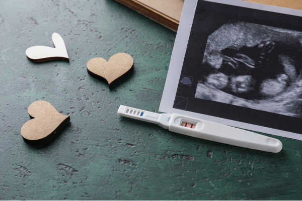 Ultrasound image with positive pregnancy test.  Wooden hearts scattered on a dark, concrete background - pregnancy fears 