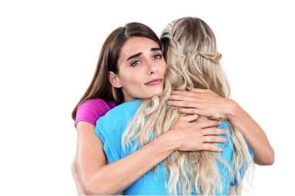 Sad young woman hugging friend on white background - comforting her despite miscarriage fears, pregnancy fears