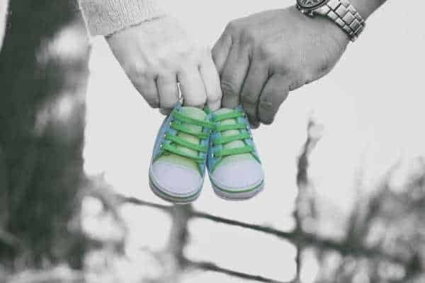 man and woman in black and white holding a pair of blue and turquoise baby shoes just like a pregnancy announcement - which miscarriage fears can cause couples to wait to announce