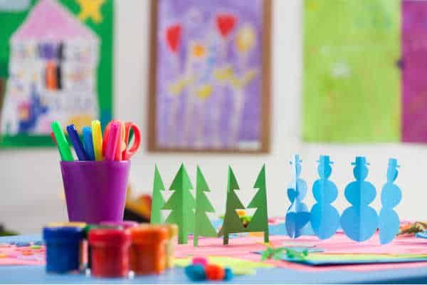 Homeschooling during the holidays with a colorful table filled with markers, paints, and paper cut-outs of trees and snowmen. 