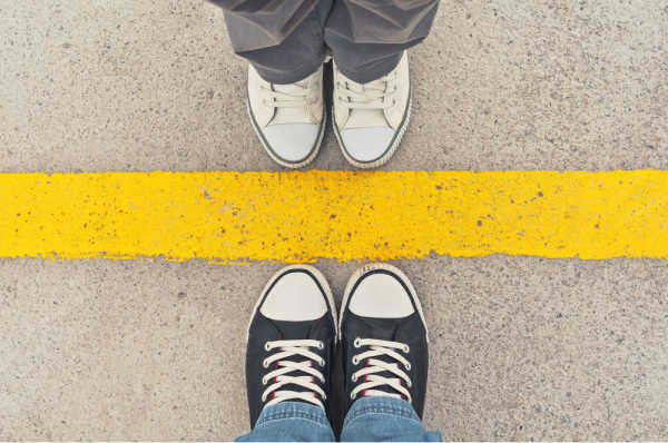 Two seats of sneaker-ed feet standing opposite a yellow line - set boundaries with family regarding homeschool