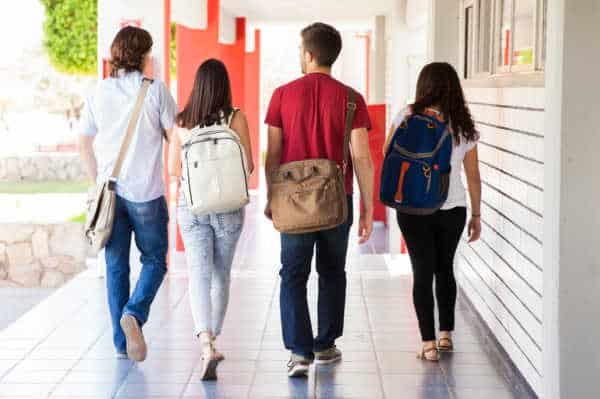 Four youth with backpacks walking along the outside of a building, symbolizing the youth who walk away from church who dislike the youth ministries