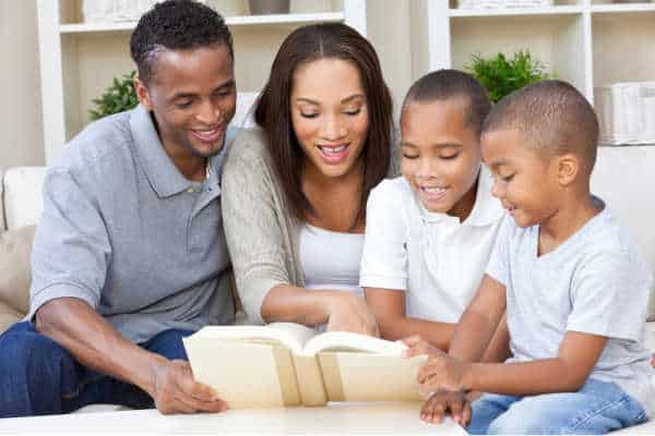 A happy African American man, woman and boys, father, mother and two sons, family sitting together at home studying the bible together because they dislike the children's ministry at church. 