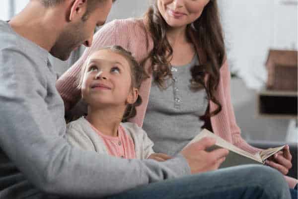 A girl looks up adoringly at her dad and mom while they study the Bible together. Even if you dislike the children's ministry, mom and dad are still the most important. 