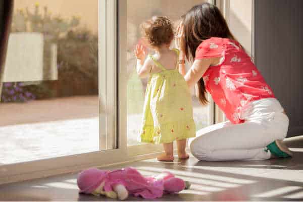 Mom and young daugther peering out the sliding glass doors - homeschooling with depression can make you feel trapped at home and unhappy