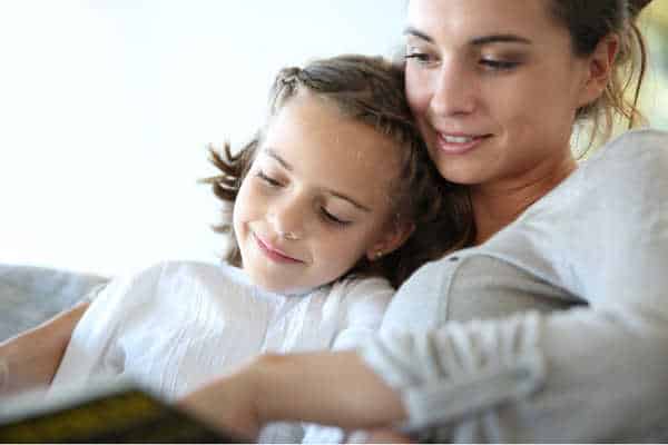 Mom with little girl reading book in sofa, taking a relaxing approach when homeschooling with depression