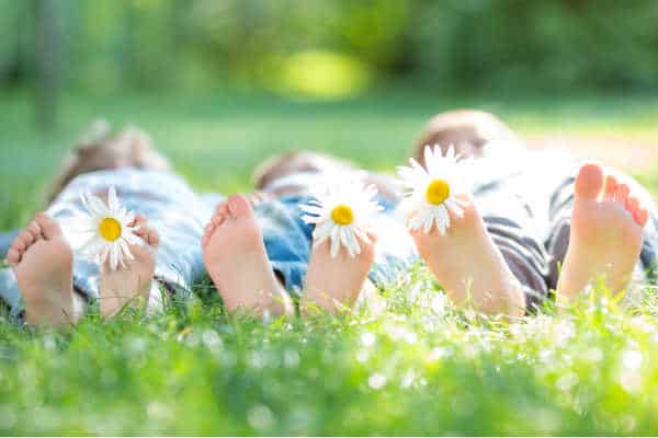 self-care for homeschool moms tip #3 is to send your kids outside.  This is illustrated by three kids laying in the sunshine and the grass.  We see mostly just their feet with each having a daisy stuck between their toes. 