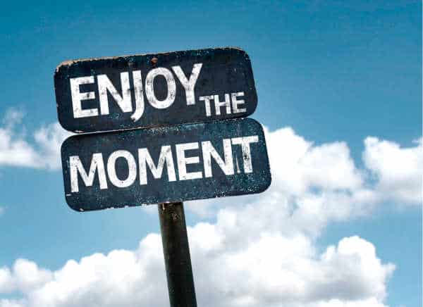 self-care for homeschool moms can look like just being in the moment. This is illustrated by a street sign that  says "Enjoy the Moment" - it is a dark blue and slightly rough around the edge with a metal pole.  The background is a bright blue sky. 