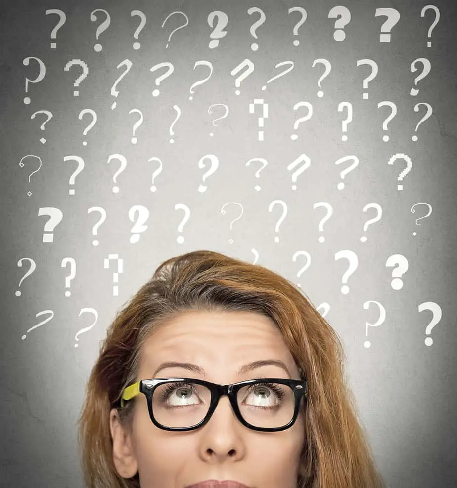 Headshot beautiful woman with puzzled face expression and question marks above her head looking up, isolated grey wall background. She is wondering ...what are devotions?