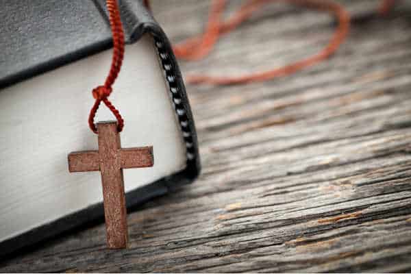 Closeup of wooden Christian cross necklace next to Holy Bible - Having a Bible is an essential to daily devotions. 