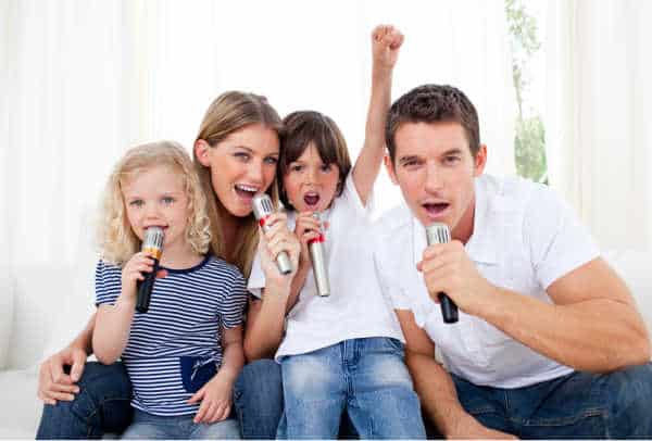 A family of four singing into microphones.  It is funny and ackward which is exactly how some families feel singing at home while trying to get kids to focus for online worship. 