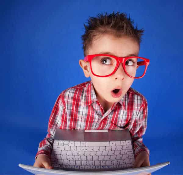 Cute little boy with spiky hair, a plaid shirt, and red oversized glasses. He is holding a computer and has a distracted and suprised look on his face - he exemplifies how hard it is to get kids to focus for online church. 