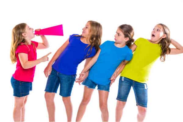 It is hard to parent a bossy child like this one. She has a megaphone and is yellng at three other little girls.  She is the smallest of the group.  They are all wearing jean shorts and then colorful tshirts. 