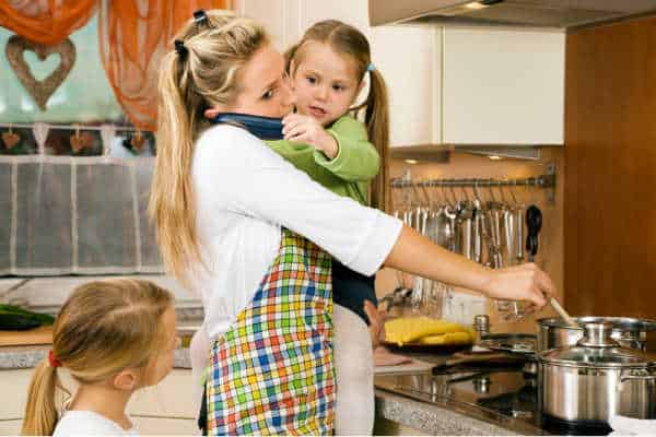 Mom overwhelmed holding a child while talking on the phone and trying to cook supper.  Modern life is so busy, family should consider the peace of the family business model as a reason to raise kids to be entrepreneurs. 