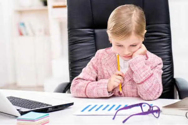 Little girl in a pink tweed suit sitting at an office desk looking at paperwork.  She is a budding entreprenuer - prepare your homeschooler to be an entreprenuer