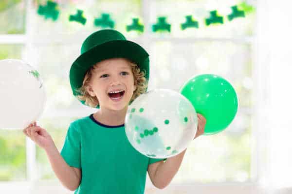 Young boy celebrating St Patrick's Day with green balloons and a garland of clover.  Perhaps he is learning about this Christian saint at church. 